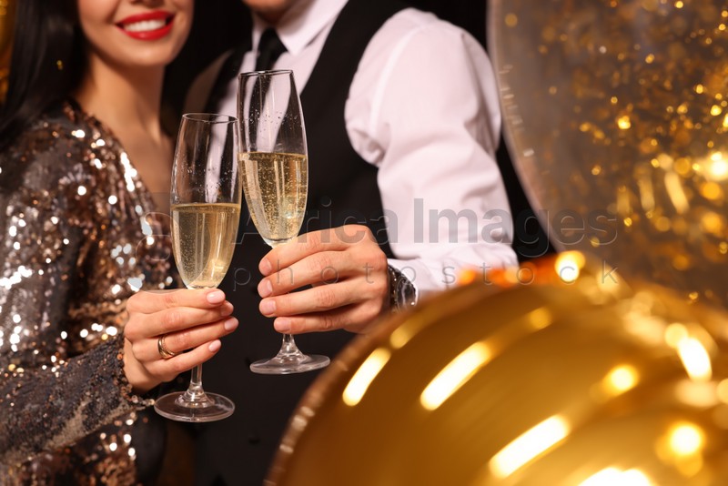 Couple with glasses of sparkling wine celebrating New Year on black background, closeup