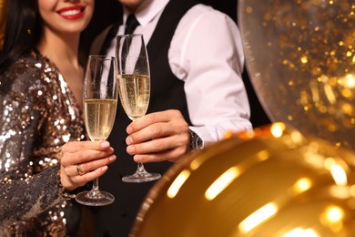 Photo of Couple with glasses of sparkling wine celebrating New Year on black background, closeup