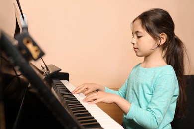 Cute little girl playing piano near beige wall. Music lesson
