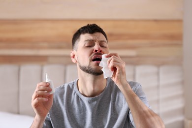 Sick man with nasal spray and paper tissue at home