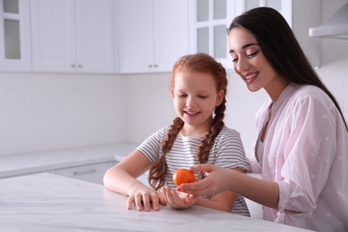 Happy girls with fresh ripe tangerine at table in kitchen