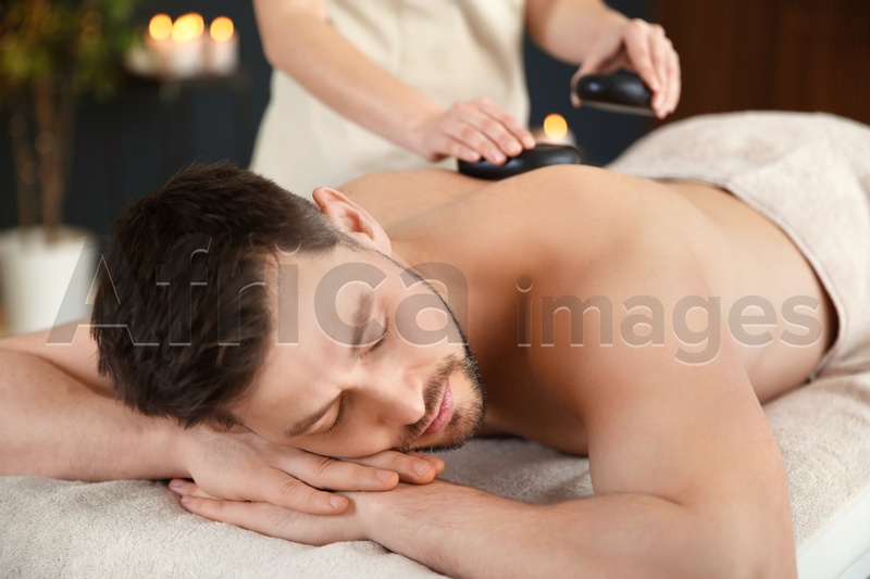 Photo of Handsome man receiving hot stone massage in spa salon