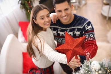 Photo of Couple decorating Christmas tree indoors, focus on star topper