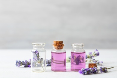 Photo of Bottles with essential oil and lavender flowers on white wooden table