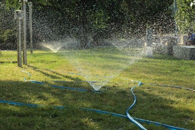 Photo of Automatic sprinkler watering green grass in park. Irrigation system