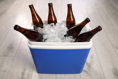 Blue plastic cool box with ice cubes and beer on wooden floor