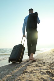Businessman with suitcase walking on beach, low angle view. Business trip
