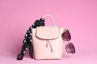 Stylish woman's backpack, scarf and sunglasses on light pink background