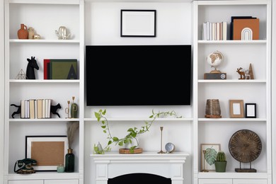Photo of Stylish shelves with different decor elements and TV set in living room. Interior design