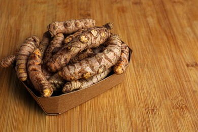 Photo of Cardboard box with whole turmeric roots on wooden table. Space for text