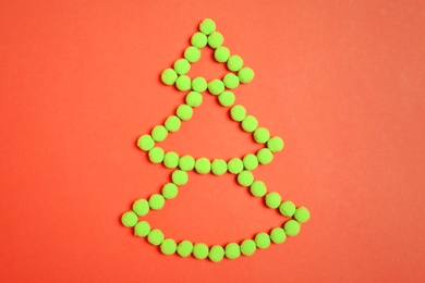 Christmas tree shape made with green fluffy balls on orange background, flat lay