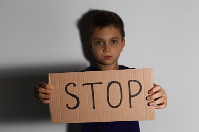 Abused little boy with sign STOP near white wall. Domestic violence concept