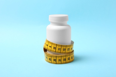 Bottle of weight loss pills with measuring tape on color background