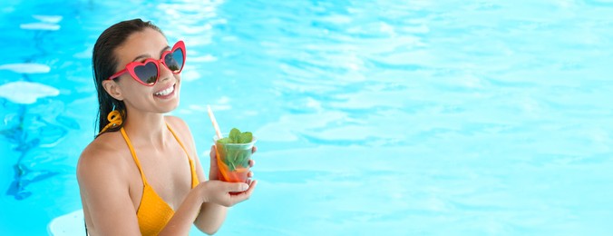 Woman with glass of refreshing drink in swimming pool, space for text. Banner design