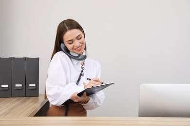 Female receptionist with clipboard talking on phone at workplace