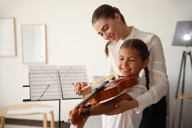 Young woman teaching little girl to play violin indoors