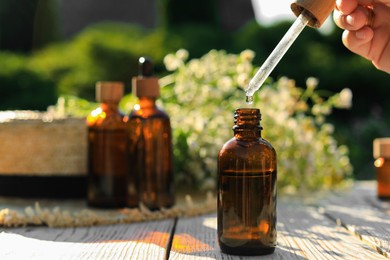 Woman dripping chamomile essential oil into bottle at white wooden table, closeup. Space for text