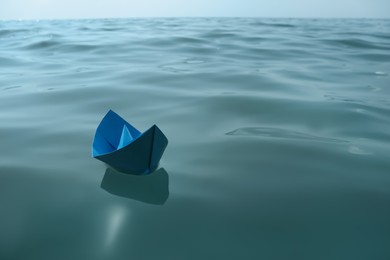Light blue paper boat floating on water surface, space for text