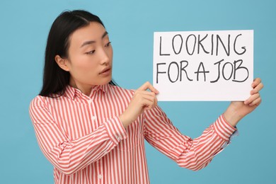 Photo of Unemployed Asian woman holding sign with phrase Looking For A Job on light blue background