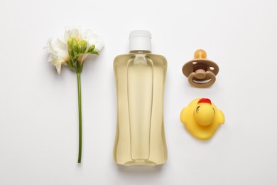 Photo of Bottle of baby oil, pacifier, toy duck and freesia on white background, flat lay