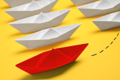 Photo of Red paper boat floating away from others on yellow background, closeup. Uniqueness concept