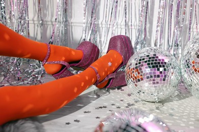 Photo of Woman in orange tights and pink high heeled shoes among disco balls indoors, closeup