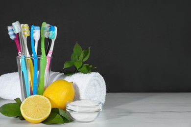 Photo of Toothbrushes, lemons and bowl of baking soda on white table against black background, space for text
