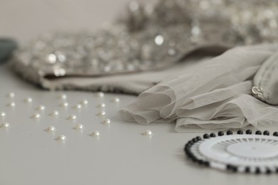 Photo of Silver fabric with paillettes, beads and pins on white table, closeup. Space for text