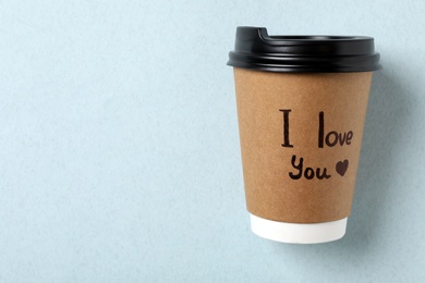 Paper cup with phrase I Love You on light blue background, top view
