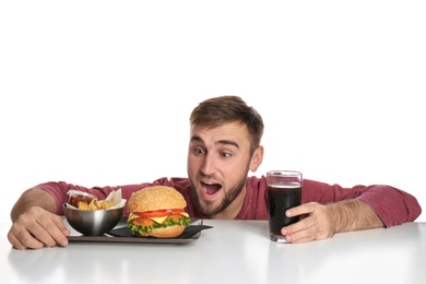 Young hungry man with glass of cola, tasty burger and French fries on white background