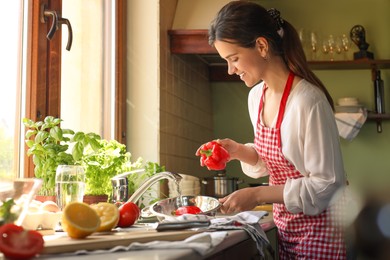 Young woman washing fresh bell peppers in kitchen sink