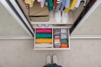 Woman near wardrobe with organized clothes and shoes indoors, top view. Vertical storage