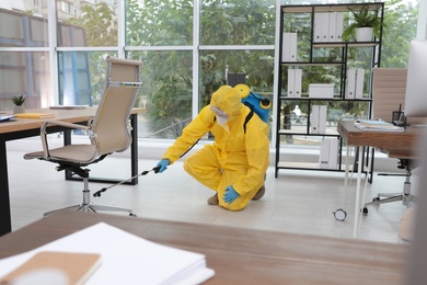 Janitor in protective suit disinfecting office to prevent spreading of COVID-19