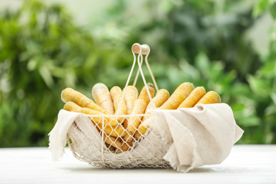 Raw yellow carrots in basket on white wooden table against blurred background