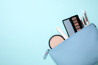 Bag with hygienic lipstick and cosmetic products on turquoise background, flat lay. Space for text
