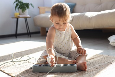 Photo of Baby girl playing with charger and power strip on floor at home. Dangerous situation