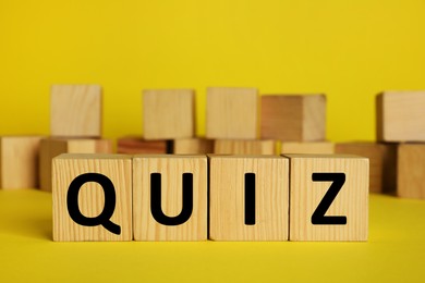 Wooden cubes with word Quiz on yellow background. Space for text