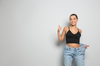 Slim woman in oversized jeans on light background, space for text. Weight loss
