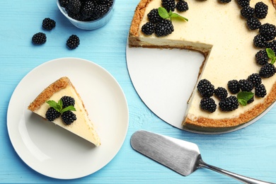 Sliced delicious cheesecake with blackberries on light blue wooden background, flat lay