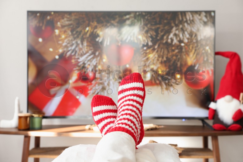 Woman in cute knitted socks watching TV at home, closeup