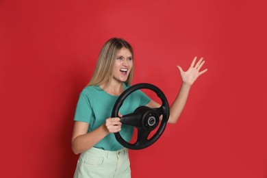 Emotional young woman with steering wheel on red background