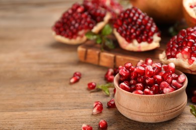 Delicious ripe pomegranate kernels in bowl on wooden table. Space for text