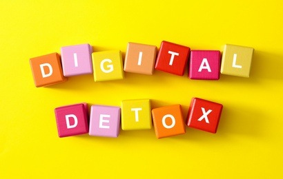 Colorful cubes with phrase DIGITAL DETOX on yellow background, flat lay