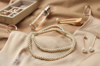 Photo of Stylish jewelry with pearls, luxury perfume and silk dress on beige fabric, closeup