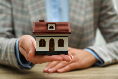 Real estate agent holding house model at wooden table, closeup