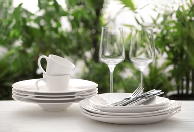 Set of clean dishware, cutlery and wineglasses on white table against blurred background