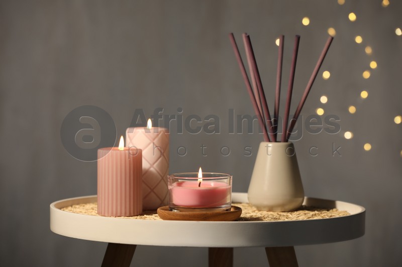 Burning candles and reed diffuser on table against grey background