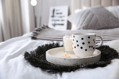 Cup of drink and burning candles on bed in room, space for text. Interior design