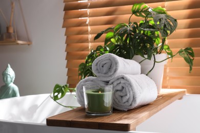 Soft towels, burning candle and green plant on bathtub in room. Interior design