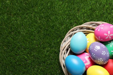 Colorful Easter eggs in decorative nest on green grass, top view. Space for text